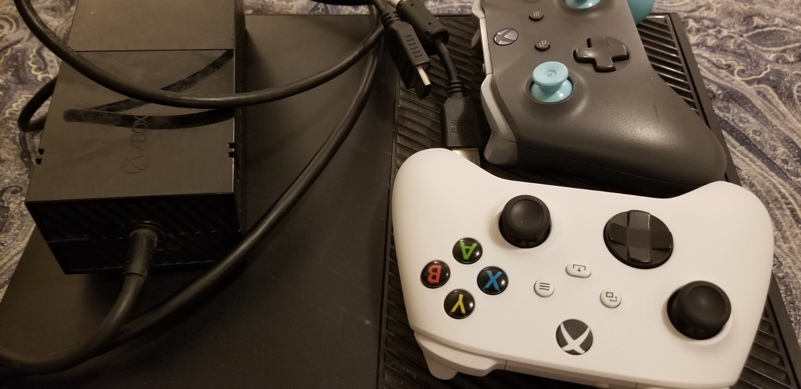 Black Xbox One Console with three wireless remotes.  Turqoise, Red, and White.